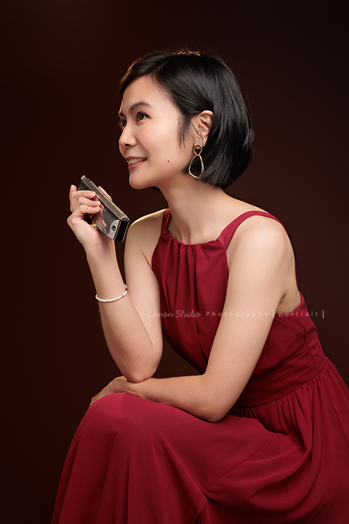 知名口琴演奏家衍華，近日為音樂形象照拍攝，緩緩展開她與音樂的對話，歷經無數舞台洗禮，屢獲殊榮並擔任評審的她，舉手投足間皆是樂音流動的痕跡，彷彿音符化形，翩然於鏡頭之中，這張是衍華身穿紅色的禮服側身坐在椅子上，手拿著口琴，沒有看鏡頭微笑的一張很美很有意境的音樂形象照！