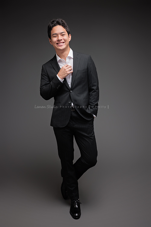 Cindy 媽麻一家來拍照，在美國念書的兒子瑋，帥氣又溫暖，一家人換上正式與休閒的服裝，每一張照片都記錄下最自然的互動與情感，這張是兒子瑋穿著西裝、一手拉著襯衫的扣子，帥氣地微笑著看著鏡頭，是一張很帥氣的個人寫真！