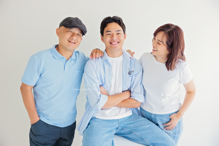 Cindy 媽麻一家來拍照，在美國念書的兒子瑋，帥氣又溫暖，一家人換上正式與休閒的服裝，每一張照片都記錄下最自然的互動與情感，這張是一家人穿藍色系的衣服，兒子瑋坐在椅子上、爸爸和媽媽站在他的兩邊，一家三口很有質感及自然的全家福寫真！