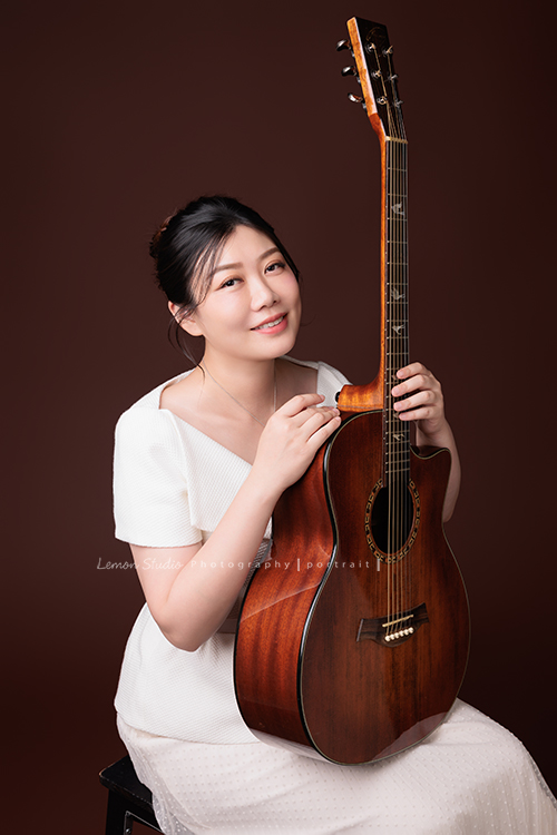 音樂治療師婷婷來拍照,拍完一套正式服裝的形象照後,她換上白色洋裝,輕輕抱著吉他入鏡,這張是音樂治療師婷婷坐在椅子上、兩手輕輕扶著放在腿上的吉他、看著鏡頭笑得很美的一張音樂形象照!