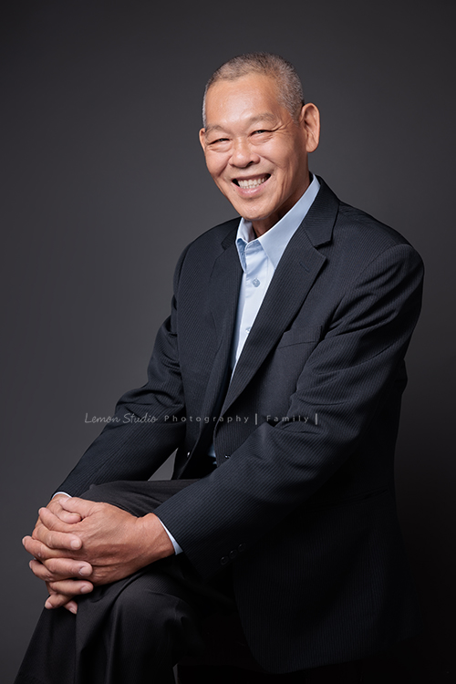 嘉倫和家人們帶著爸爸媽媽一起來拍照，兄弟姊妹的另一半與孩子們也都到齊，這天帥氣的伯父特地穿上西裝，和家人們留下不同組合的畫面，這張是帥氣的伯父坐在椅子上、兩手抱著腳、看著鏡頭笑容很燦爛的個人照！