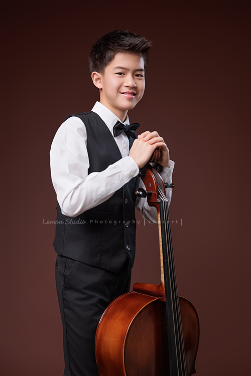 暟與大提琴，一同走進鏡頭，隨著光影與姿態變化，每一個角度，都映出暟不同的氣息與神韻，這張是暟站著雙手扶在大提琴上、帶著自信看著鏡頭微笑的一張很帥氣的音樂寫真照！