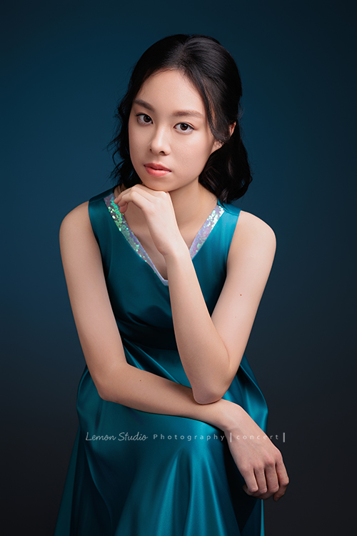 高一的珊為了即將來到的音樂會拍照，主修鋼琴的她氣質清新、表現亮眼，穿著藍色禮服的珊，舉手投足都流露出優雅與自信，這張是珊坐在椅子上，一手一邊靠著腳一邊放在下巴下、很優雅地看著鏡頭的一張音樂會寫真照！