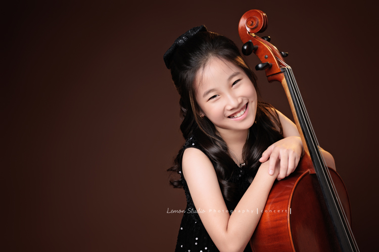 Tristan & Natalie兄妹倆帶著大提琴來拍照，和同學們一起為音樂會做準備，兄妹倆活潑又有默契，這次大家準備的團服也格外亮眼，每一張照片都展現出屬於他們自己的風格與魅力，這張是Natalie雙手扶在大提琴上，Natalie看著鏡頭微笑的大提琴音樂寫真照！