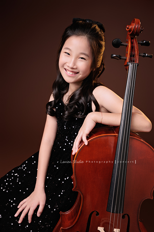 Tristan & Natalie兄妹倆帶著大提琴來拍照，和同學們一起為音樂會做準備，兄妹倆活潑又有默契，這次大家準備的團服也格外亮眼，每一張照片都展現出屬於他們自己的風格與魅力，這張是Natalie坐在大提琴旁、一手靠著大提琴，Natalie看著鏡頭微笑的大提琴音樂寫真照！