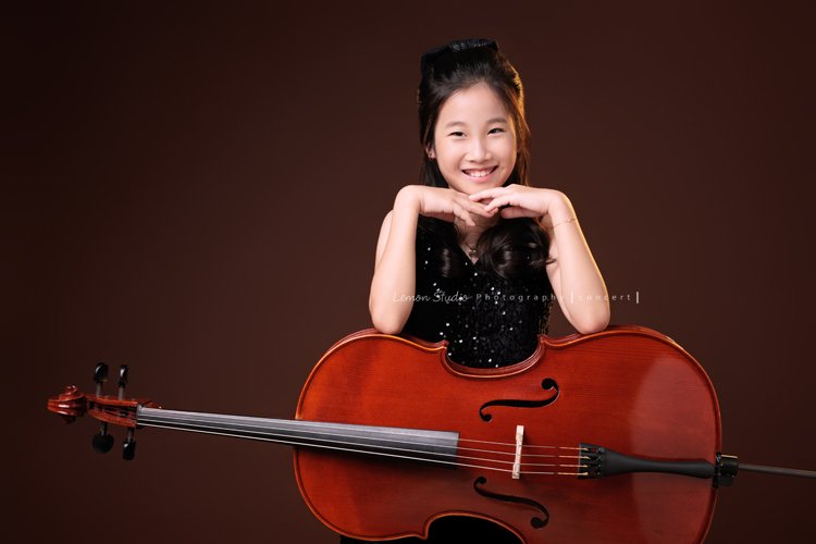 Tristan & Natalie兄妹倆帶著大提琴來拍照，和同學們一起為音樂會做準備，兄妹倆活潑又有默契，這次大家準備的團服也格外亮眼，每一張照片都展現出屬於他們自己的風格與魅力，這張是Natalie雙手放在大提琴上雙手扶在下巴處，看著鏡頭微笑的大提琴音樂寫真照！