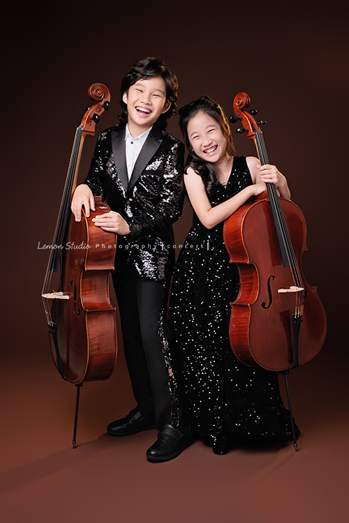 Tristan & Natalie兄妹倆帶著大提琴來拍照，和同學們一起為音樂會做準備，兄妹倆活潑又有默契，這次大家準備的團服也格外亮眼，每一張照片都展現出屬於他們自己的風格與魅力，這張是Tristan & Natalie兩人一起站著各扶著自己的大提琴，兩人笑得很開心的大提琴音樂會寫真合照！