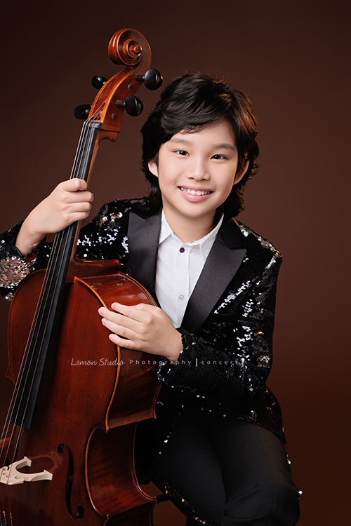 Tristan & Natalie兄妹倆帶著大提琴來拍照，和同學們一起為音樂會做準備，兄妹倆活潑又有默契，這次大家準備的團服也格外亮眼，每一張照片都展現出屬於他們自己的風格與魅力，這張是Tristan 坐在椅子上雙手扶著大提琴，Tristan看著鏡頭微笑的大提琴音樂寫真照！