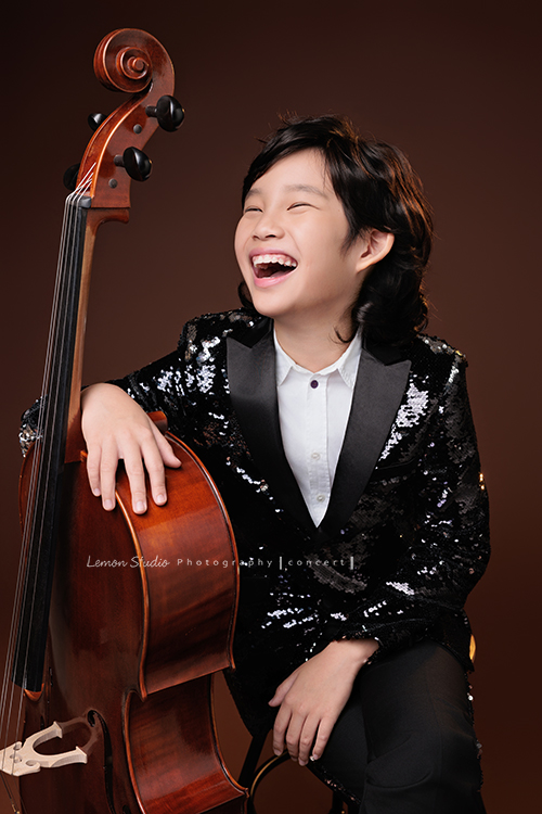 Tristan & Natalie兄妹倆帶著大提琴來拍照，和同學們一起為音樂會做準備，兄妹倆活潑又有默契，這次大家準備的團服也格外亮眼，每一張照片都展現出屬於他們自己的風格與魅力，這張是Tristan坐在椅子上一手扶著大提琴，Tristan笑的很開心的當下大提琴音樂寫真照！