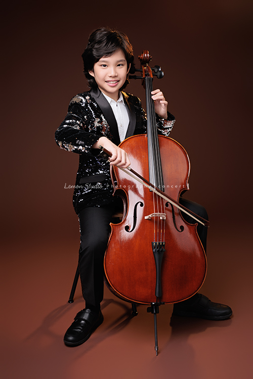 Tristan & Natalie兄妹倆帶著大提琴來拍照，和同學們一起為音樂會做準備，兄妹倆活潑又有默契，這次大家準備的團服也格外亮眼，每一張照片都展現出屬於他們自己的風格與魅力，這張是Tristan坐在椅子上正拉著大提琴，看著鏡頭微笑的大提琴音樂寫真照！