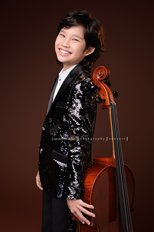 Tristan & Natalie兄妹倆帶著大提琴來拍照，和同學們一起為音樂會做準備，兄妹倆活潑又有默契，這次大家準備的團服也格外亮眼，每一張照片都展現出屬於他們自己的風格與魅力，這張是Tristan背靠著大提琴，Tristan看著鏡頭笑得很燦爛的大提琴音樂寫真照！