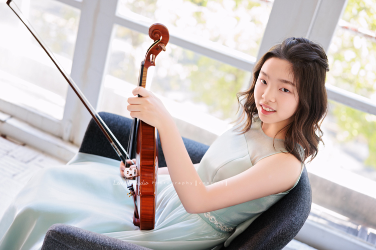 這是 Audrey 第三次來拍音樂會寫真,今年的她,又長大了一些,越來越美,也越來越有屬於自己的氣質,這張是Audrey穿著淡綠色的小禮服,坐在窗邊的椅子上一手拿著小提琴、一手拿著弓側身並看著鏡頭微笑的一張很美的小提琴音樂會寫真!