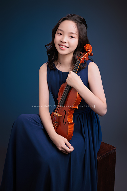 這是 Audrey 第三次來拍音樂會寫真,今年的她,又長大了一些,越來越美,也越來越有屬於自己的氣質,這張是Audrey穿著藍色的小禮服,坐在箱子上兩手拿著小提琴在身前、看著鏡頭微笑的一張很美的小提琴音樂會寫真!