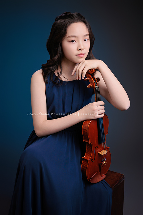 這是 Audrey 第三次來拍音樂會寫真,今年的她,又長大了一些,越來越美,也越來越有屬於自己的氣質,這張是Audrey穿著藍色的小禮服,坐在箱子上兩手拿著小提琴、一手放在下巴下、優雅地看著鏡頭的一張很美的小提琴音樂會寫真!