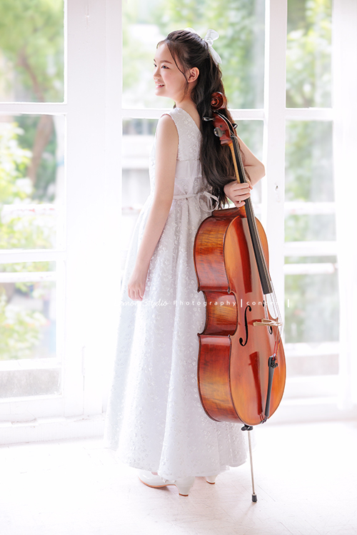 Candice帶著她的大提琴來拍攝音樂寫真,白色的小禮服在光線中顯得輕柔,深棕色的大提琴靜靜陪在身旁,多了一份沉穩,也多了一份優雅,這張是Candice背對著鏡頭一手扶著在身體後側的大提琴,沒有看鏡頭臉向著側面微笑的音樂寫真照!