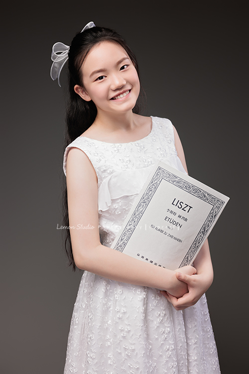 Candice帶著她的大提琴來拍攝音樂寫真,白色的小禮服在光線中顯得輕柔,深棕色的大提琴靜靜陪在身旁,多了一份沉穩,也多了一份優雅,這張是Candice雙手拿著樂譜看著鏡頭微笑的音樂寫真照!