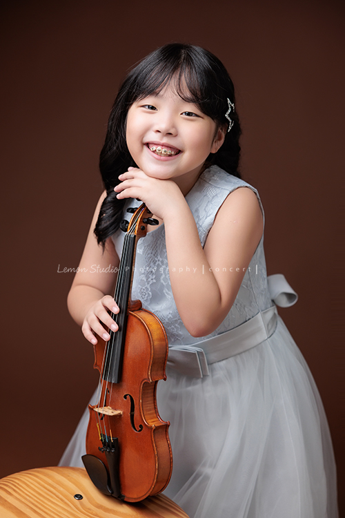 Jonathan & Chloe兄妹倆來拍提琴音樂寫真，再次站在鏡頭前，今年的 Jonathan 明顯長大了許多，Chloe非常活潑可愛，主動幫忙帶動現場氣氛，讓整個拍攝過程溫馨又美好，這張是Chloe手靠在提琴上、頭輕靠著放在提琴上的手、看著鏡頭笑得很甜美的一張音樂寫真照！