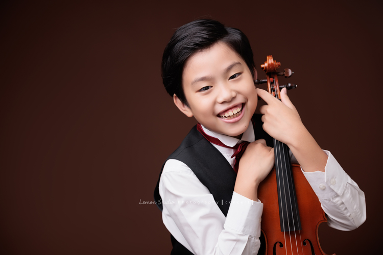 Jonathan & Chloe兄妹倆來拍提琴音樂寫真，再次站在鏡頭前，今年的 Jonathan 明顯長大了許多，Chloe非常活潑可愛，主動幫忙帶動現場氣氛，讓整個拍攝過程溫馨又美好，這張是Jonathan兩手拿著提琴、笑得很開心並看著鏡頭的音樂寫真照！