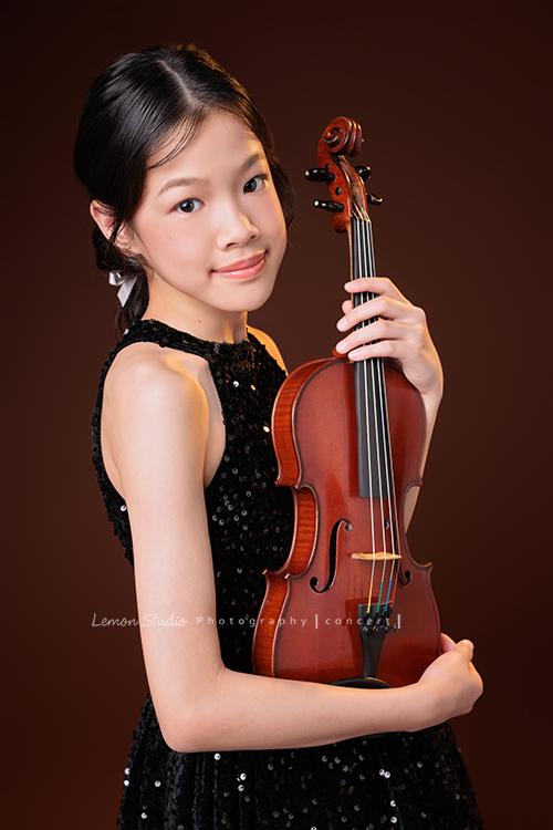 音樂班的 Isha要畢業了,這次拍攝準備了不同的禮服,每一張相片裡的Isha都好美,在音樂班的薰陶下,音樂好像早就成為她的日常,一個眼神、一個動作,都自然地帶著音樂的氣息,她要帶著這份從音符裡長出的自信,走向人生的下一個新階段,這張是 Isha穿著黑色小禮服站在鏡頭前,雙手抱著提琴、看著鏡頭微微地笑的一張音樂班畢業音樂寫真紀念照!
