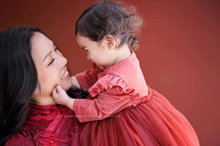 Kim媽麻一家第二次來到台灣，因為女兒Lilia真的很喜歡台灣，這個聖誕假期，他們又一起飛來過節，也因為在美國的左鄰右舍、朋友們一致推薦來檸檬巷館拍照，幾個月前Kim媽麻就先預約好了拍照行程，這張是Kim媽麻和小女兒Lenora互動的紀錄合照之一，Lenora正在捏玩媽麻的臉頰，Lenora頭髮自然捲，笑起來超可愛的！