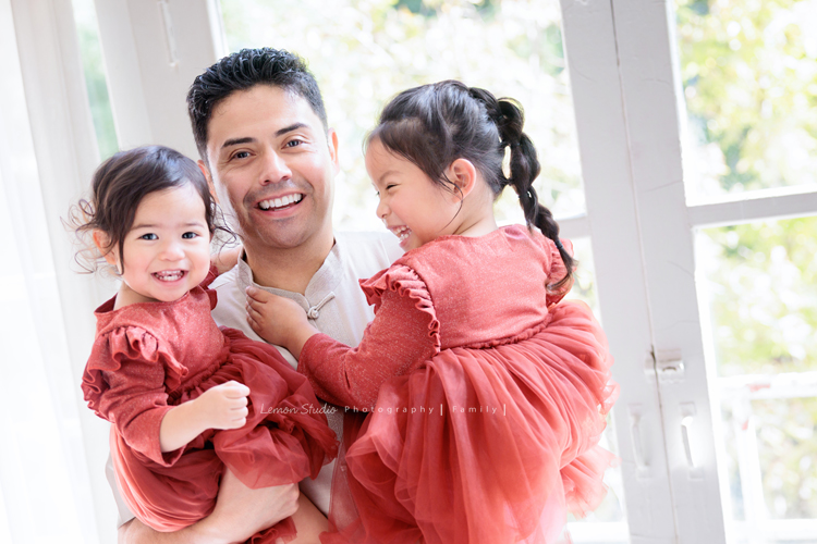 Kim媽麻一家第二次來到台灣，因為女兒Lilia真的很喜歡台灣，這個聖誕假期，他們又一起飛來過節，也因為在美國的左鄰右舍、朋友們一致推薦來檸檬巷館拍照，幾個月前Kim媽麻就先預約好了拍照行程，這張是爸拔兩手各抱著Lilia和Lenora，三人可愛的父女合照，Lenora笑得好甜美啊！