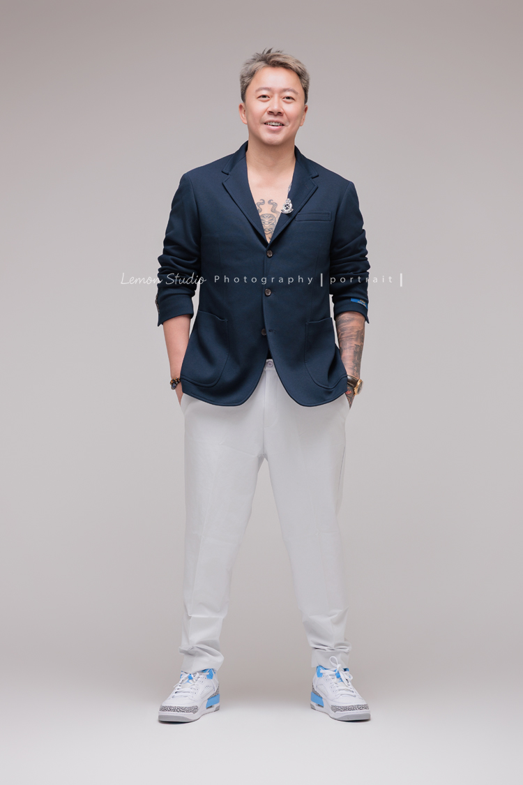 巧靈公司的團隊，每一年都會依尾牙的主題來拍團隊形象照，今年走海軍風，整體走一個優雅又俐落的路線，這張是一位男士，穿著藍色西裝外套及白長褲、白布鞋，雙手放在口袋、看著鏡頭微笑的一張，很有質感又帥氣的形象照！