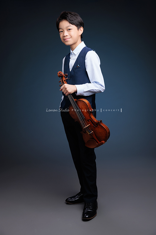 喆即將從國小弦樂團畢業，和同學們一起來拍音樂寫真照，拍照當天在現場很認真地拉琴，我們也不知不覺成了他的粉絲，這張是喆一手拿著提琴、一手放口袋，身體稍微側站著、轉頭過來看著鏡頭沈穩且有自信地微笑著的一張全身的音樂寫真照！