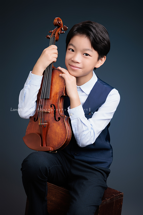 喆即將從國小弦樂團畢業，和同學們一起來拍音樂寫真照，拍照當天在現場很認真地拉琴，我們也不知不覺成了他的粉絲，這張是喆坐著提琴在身體前方、喆雙手扶著提琴看著鏡頭微笑的音樂寫真照！