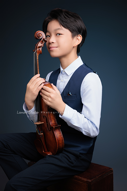 喆即將從國小弦樂團畢業，和同學們一起來拍音樂寫真照，拍照當天在現場很認真地拉琴，我們也不知不覺成了他的粉絲，這張是喆坐著提琴在身體前方、喆雙手扶著提琴側身微轉頭過來看著鏡頭很有自信地微笑著的一張很帥氣的音樂寫真照！