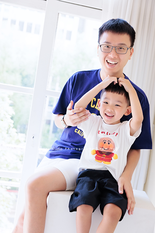 彥鈞爸拔一家來拍家庭寫真，媽麻肚子裡有可愛的二寶，哥哥開朗又活潑，和爸拔媽麻的互動充滿笑聲，這張是哥哥坐在爸拔前面、兩人正在互動、兩人也正看著鏡頭微笑著的一張很可愛的親子互動紀錄照！