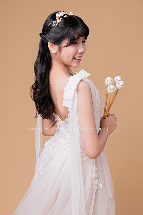 音樂班的 Lily畢業前來拍音樂班畢業音樂寫真照，Lily的活潑與大方在鏡頭前自然流露，這張是Lily穿著一襲白色的禮服、拿著馬林巴木琴槌在身體前方、稍微背對著鏡頭、轉頭過來看向前方沒有看鏡頭笑得很甜美的一張音樂班畢業音樂寫真照！