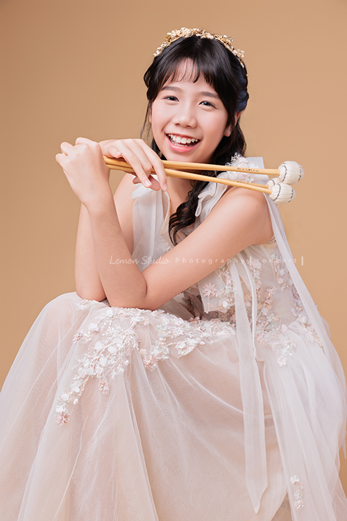 音樂班的 Lily畢業前來拍音樂班畢業音樂寫真照，Lily的活潑與大方在鏡頭前自然流露，這張是Lily穿著一襲白色的禮服、坐著拿著馬林巴木琴槌在身體前方、看著鏡頭笑得很燦爛甜美的一張音樂班畢業音樂寫真照！