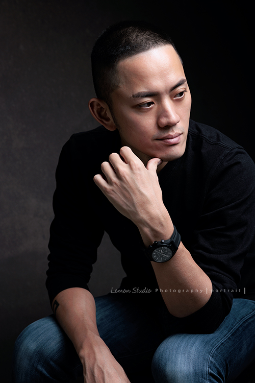 品牌創辦人 Mike來拍形象照，低調、沉穩，帶著一點故事感，也隱約帶著哲學及神秘感的形象照，這張是Mike坐在椅子上、一手手指摸著下巴、看著旁邊沒有看鏡頭的形象照！是一張低調很有質感的形象照！