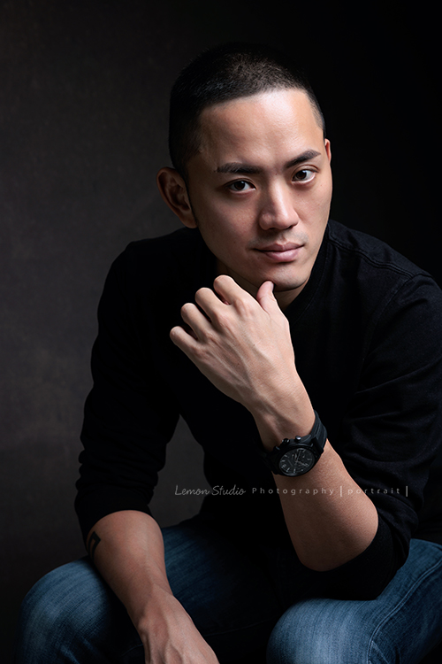 品牌創辦人 Mike來拍形象照，低調、沉穩，帶著一點故事感，也隱約帶著哲學及神秘感的形象照，這張是Mike坐在椅子上、一手的手指摸著下巴、酷酷地看著鏡頭的形象照！是一張低調很有質感的形象照！