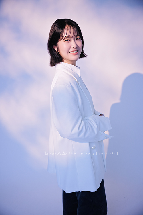 講師Tiffany來拍照，這次我們一起整理出帶點日韓系的風格，有些細微的表情與狀態，很耐看，這張是Tiffany身穿白色外套，雙手放在身體前方、側身轉過頭來看著鏡頭微笑的形象照！