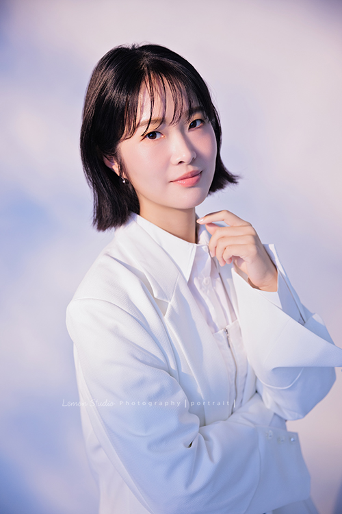 講師Tiffany來拍照，這次我們一起整理出帶點日韓系的風格，有些細微的表情與狀態，很耐看，這張是Tiffany身穿白色外套，一手放在身體前方、另一手在臉下方、有點酷酷地看著鏡頭的形象照！