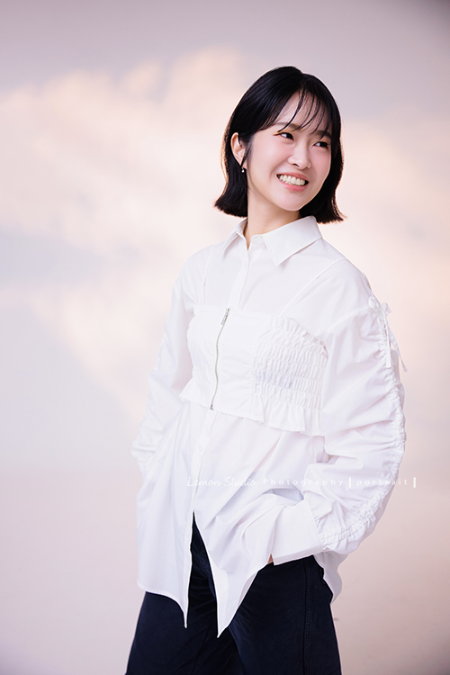 講師Tiffany來拍照，這次我們一起整理出帶點日韓系的風格，有些細微的表情與狀態，很耐看，這張是Tiffany身穿白色外套，雙手放在口袋裡、身體很自然地站著、看著旁邊很放鬆地微笑著的形象照！