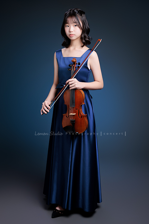 岑即將從國小弦樂團畢業,這一天,我們拍下了許多不同樣子的岑,把這些輕輕停留的瞬間,就讓相片替她好好留住,這張是岑身穿藍色小禮服、手拿著提琴及弓、沈穩地看著鏡頭的一張全身的音樂寫真照!