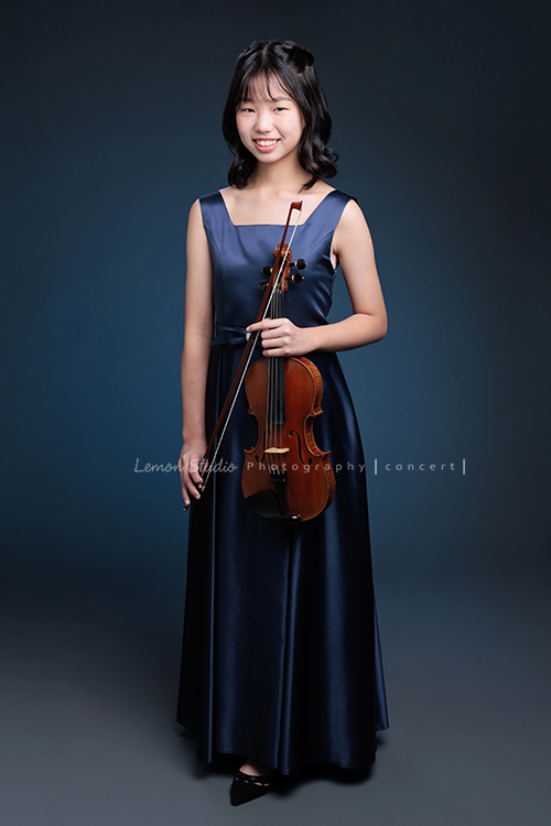 岑即將從國小弦樂團畢業,這一天,我們拍下了許多不同樣子的岑,把這些輕輕停留的瞬間,就讓相片替她好好留住,這張是岑身穿藍色小禮服、手拿著提琴及弓、微笑地看著鏡頭的一張全身的音樂寫真照!