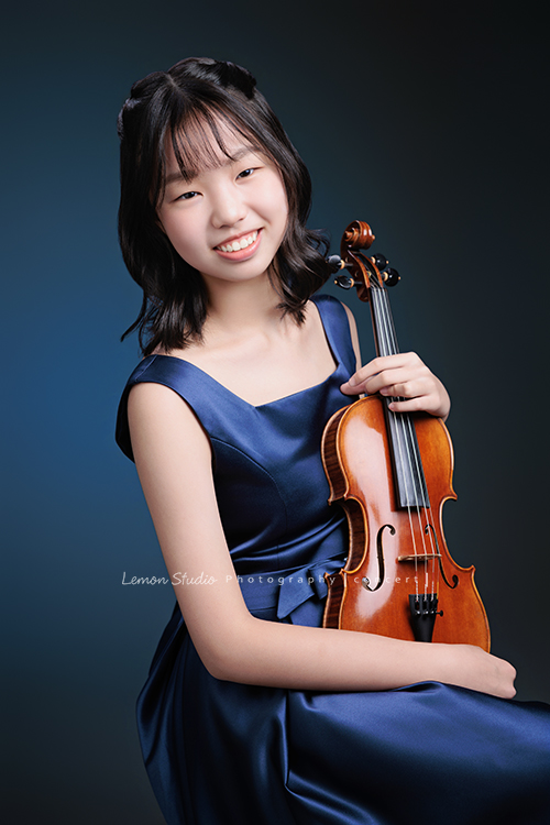 岑即將從國小弦樂團畢業,這一天,我們拍下了許多不同樣子的岑,把這些輕輕停留的瞬間,就讓相片替她好好留住,這張是岑身穿藍色小禮服、坐在椅子上雙手拿著提琴,笑容很甜美看著鏡頭的一張音樂寫真照!