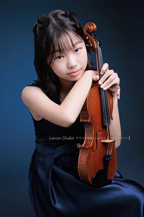 岑即將從國小弦樂團畢業,這一天,我們拍下了許多不同樣子的岑,把這些輕輕停留的瞬間,就讓相片替她好好留住,這張是岑身穿藍色小禮服、坐在椅子上兩手扶著提琴、頭輕輕地看在手上、自信且沈穩地微笑、並看著鏡頭的一張音樂寫真照!