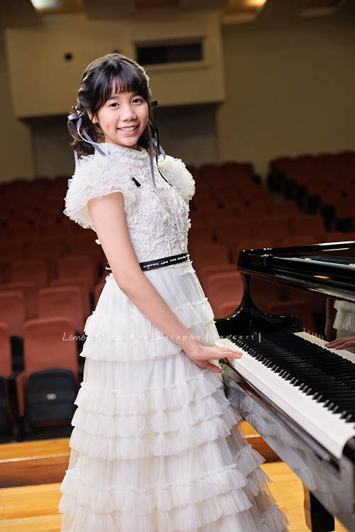 音樂班的 Lily畢業前來拍音樂班畢業音樂寫真照，Lily的活潑與大方在鏡頭前自然流露，這張是Lily穿著一襲可愛的白色禮服、站在鋼琴旁手輕輕放在琴鍵上、看著鏡頭笑得很甜美的一張音樂班畢業音樂寫真照！