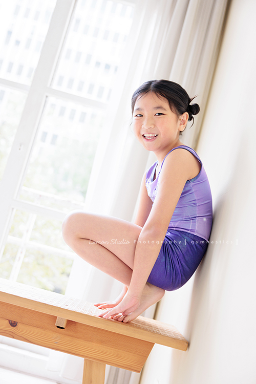 Vivien媽麻一家幾乎每年都會來拍照,三個孩子都在自己喜歡的領域裡成長著,這次小妹 Tiana帶著體操服來拍照,這張是Tiana靠著牆壁蹲在木椅上、轉頭過來甜美地看著鏡頭笑得很開心的模樣,是一張很可愛的體操運動寫真!