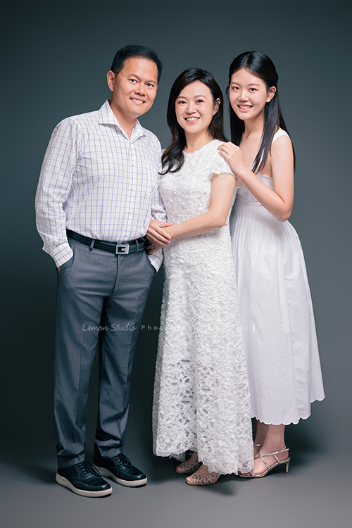 Irene媽麻一家暑假回台灣時來拍攝家庭照，今天先來分享一家三口的家庭照，Irene媽麻特別準備了白色系洋裝，一家三口在 Amber 即將踏入大學前，留下這段屬於一家人的珍貴時光，這張是Irene媽麻一家在灰背景拍的棚燈的全家福，Irene媽麻站在中間，爸拔和Amber站在她的兩旁，兩人的手都搭在Irene媽麻身上！一家人微笑著看著鏡頭！是一張很美很自然的全家福寫真！